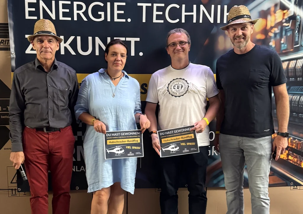 Vier Personen posieren mit  Gewinnspiel-Urkunden vor einem Energietechnik Banner.