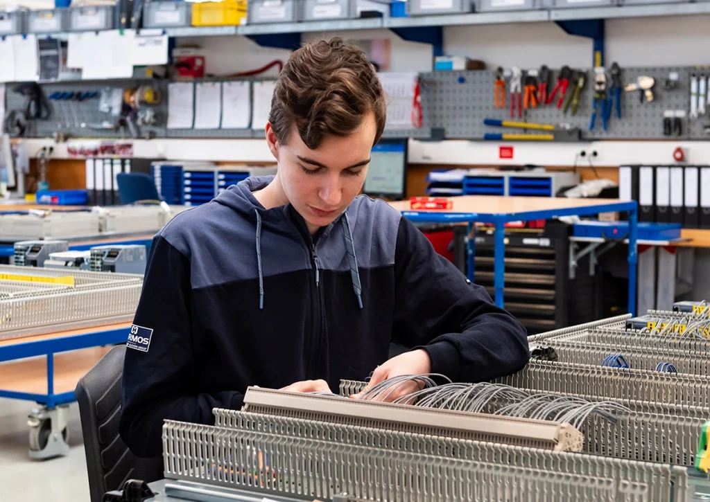 Junger Auszubildender montiert konzentriert elektrische Bauteile an einem Schaltschrank-Arbeitsplatz.