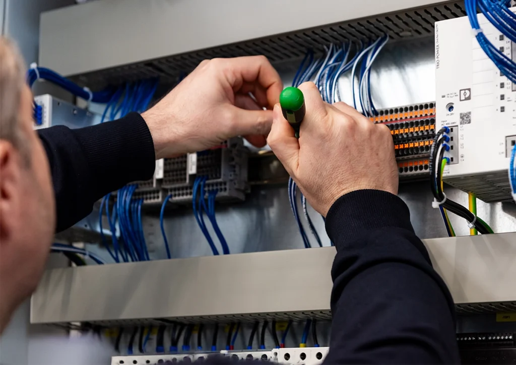 Nahaufnahme eines Elektronikers bei der Verdrahtung und Installation von Steuerungstechnik im Schaltschrank.
