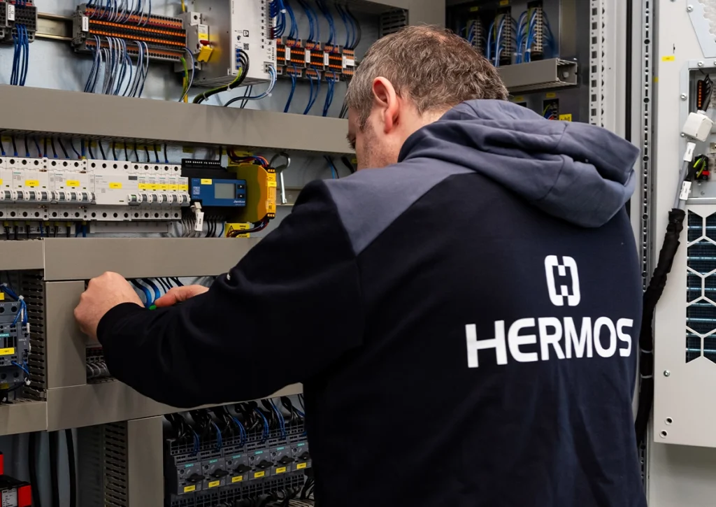 Elektroniker arbeitet an einem geöffneten Schaltschrank mit komplexer Verdrahtung und Steuerungskomponenten.
