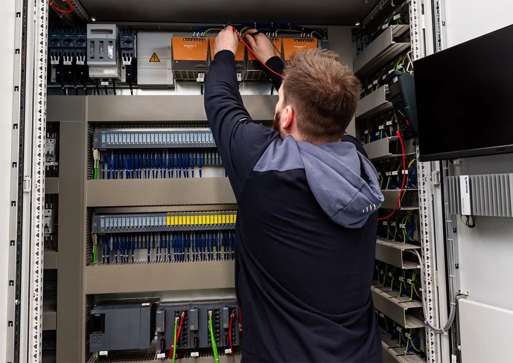 Gruppenleiter arbeitet an einem geöffneten Schaltschrank und prüft elektrische Komponenten und Verdrahtungen.