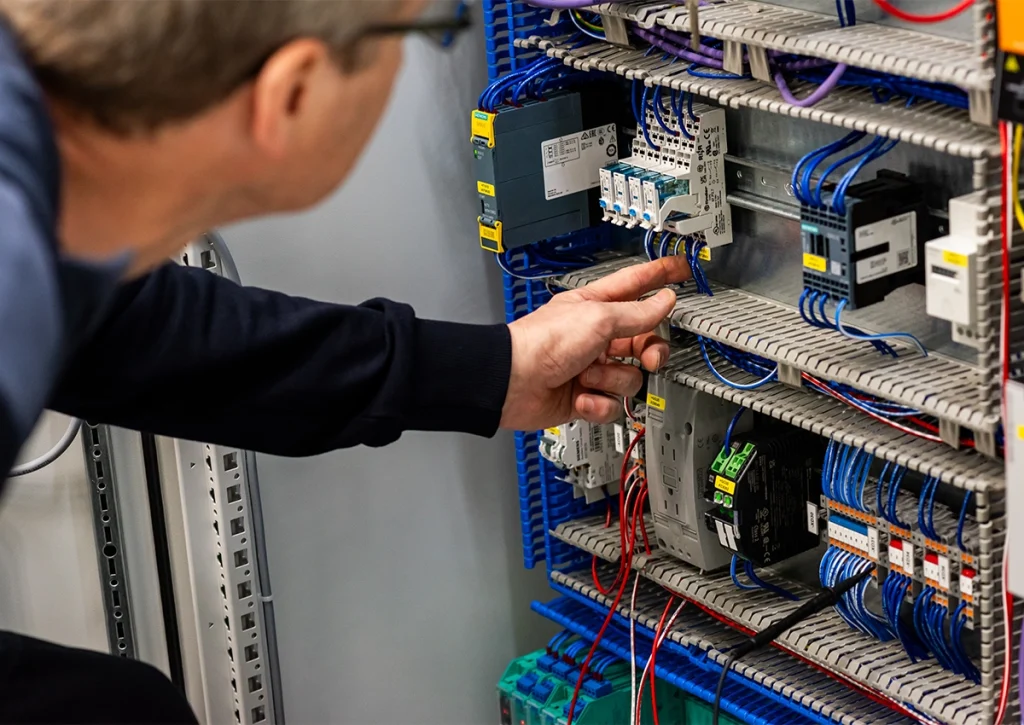 Fachkraft prüft elektrische Komponenten und Verdrahtungen innerhalb eines geöffneten Schaltschranks.